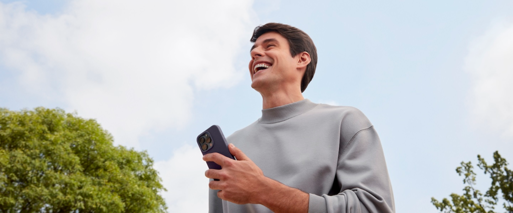 Homem sorrindo em um parque com celular na mão